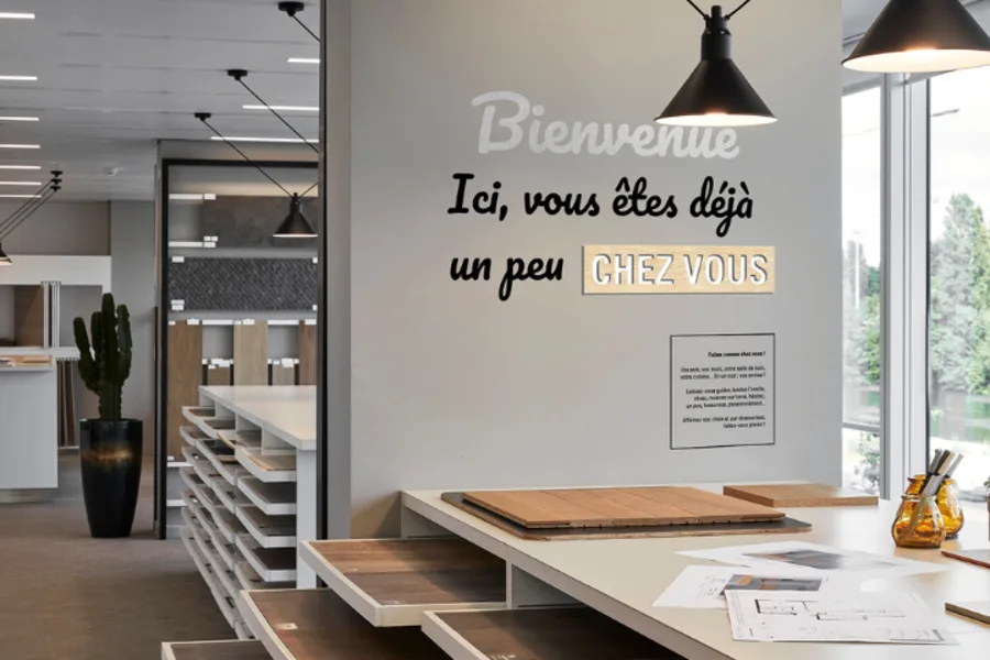 Photo du showroom Kaufman Broad de Courbevoie avec différentes palettes de matériaux pour personnaliser votre futur logement et la phrase inscrite sur un mur :
"Bienvenue
Ici, Vous êtes déjà un peu chez vous"