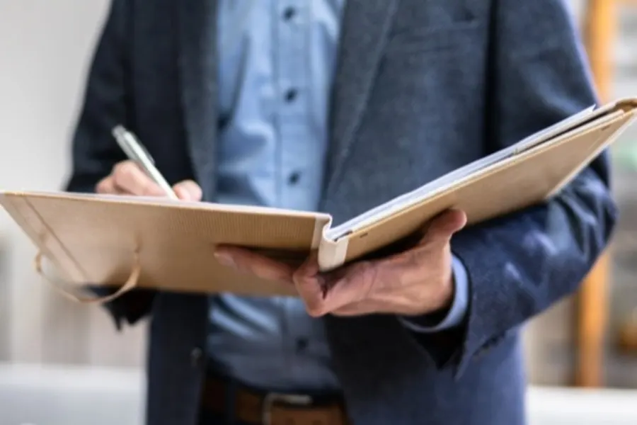 Un homme tenant un cahier sur lequel il note s'il y a des erreurs, ou non, qui on était commissent lors de l'achat d'un bien neuf.