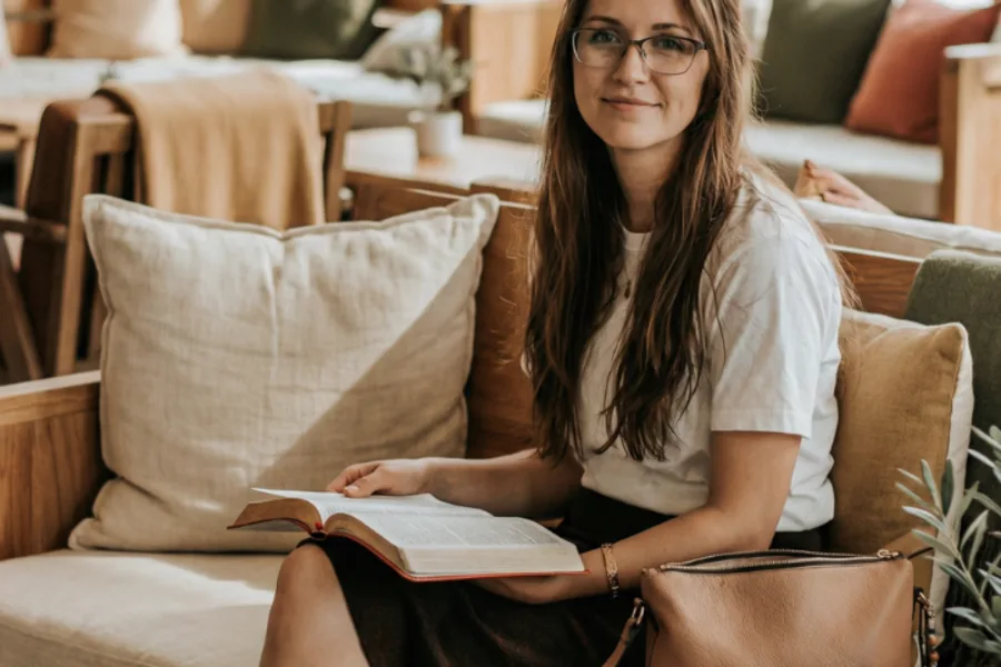 Une femme est assise dans son canapé et lit un livre.