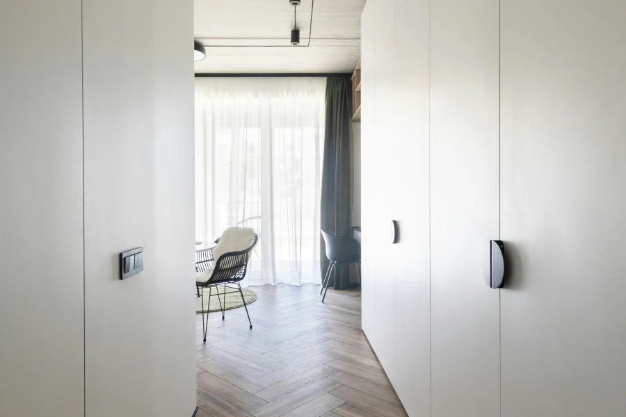 Couloir avec un plancher en bois et des murs blancs menant vers une chambre illuminé depuis la lumière naturelle provenant des fenêtres
